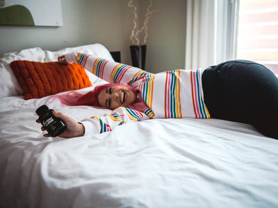 A girl is happily lying on the bed while holding a bottle of Sunday Scaries CBD Gummies