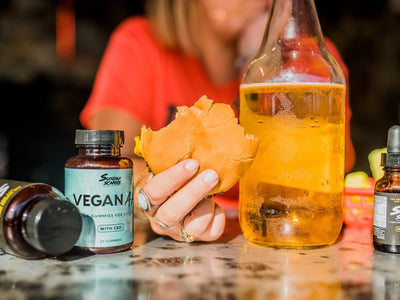 A woman holds a cheeseburger next to CBD gummies and a beer wondering if it's safe to mix CBD edibles and alcohol