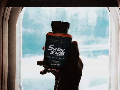 A Sunday Scaries gummies bottle in front of an airplane window showing you can take CBD edibles on an airplane
