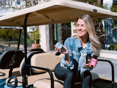 A woman in a golf cart holds up a CBD product in one hand and CBG products in the other showing the differences