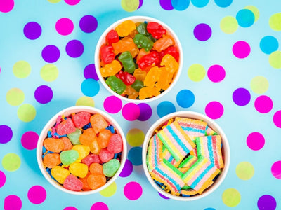 Gummies, candy and gumdrops in separate cups showing the difference between CBD and THC edibles