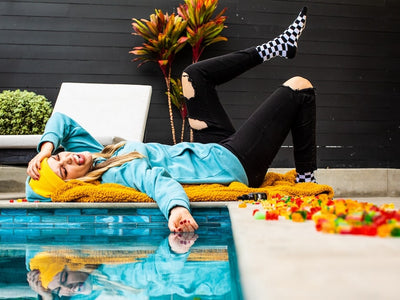 A woman lies hungover next to her pool and a pile of hangover gummies with CBD