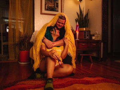 A boyfriend with a blanket over his head hugs his girlfriend and tells her what strength CBD oil to use for sleep