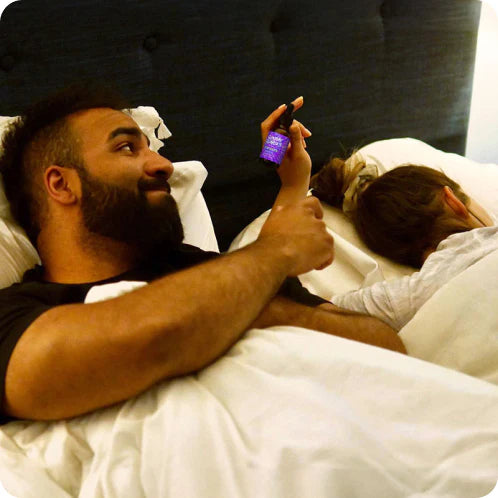 A wife shares a bottle of Sunday Scaries CBD sleep oil with her husband in bed