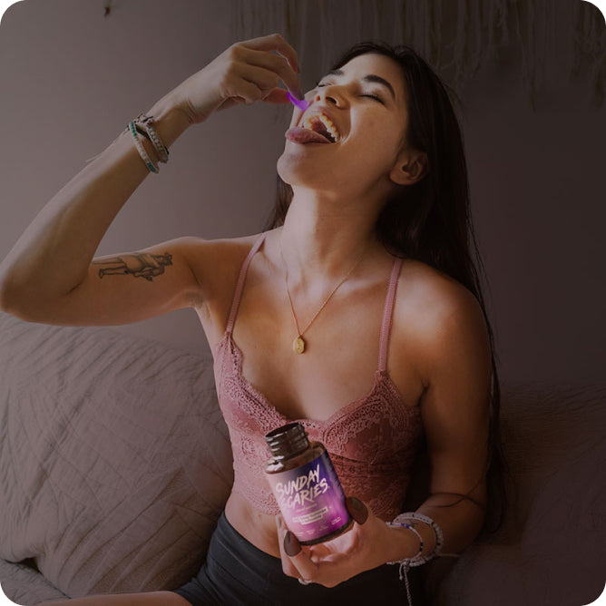 A woman eats a purple THC gummy before going to bed while holding the Sunday Scaries bottle