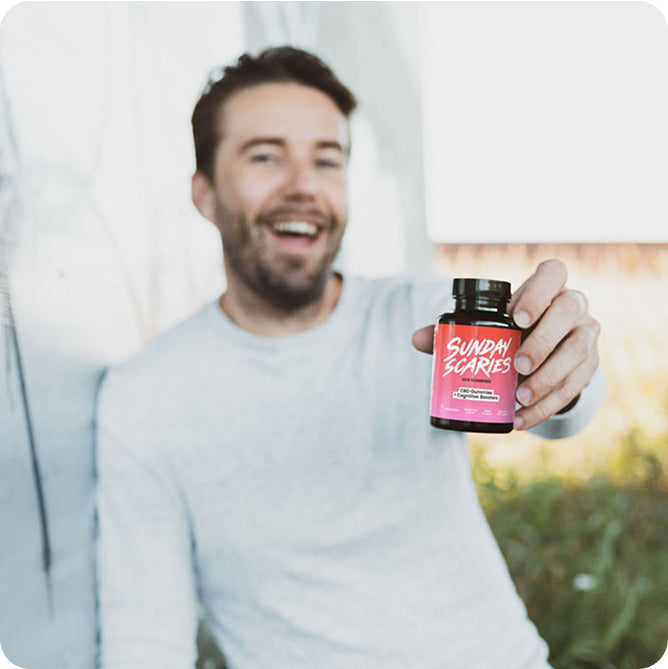 A man in a white shirt holds out a bottle of Sunday Scaries focus edition gummies