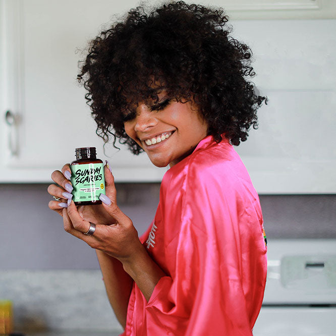 Woman holding a bottle of Sunday Scaries vegan gummies in a kitchen setting