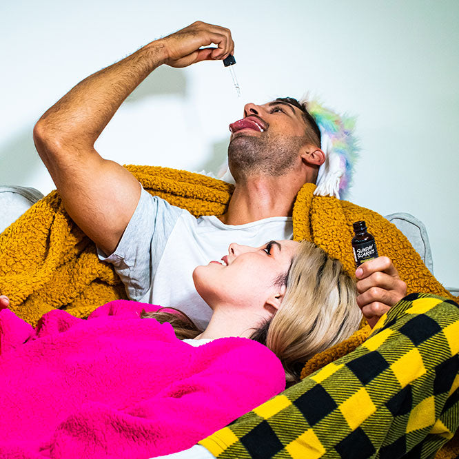 A couple cuddles on the couch while the man drops some CBD oil on his tongue