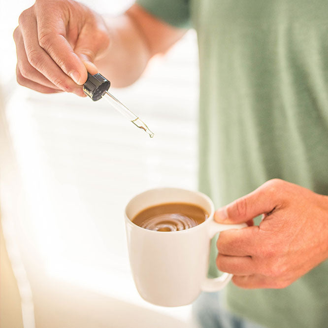 A man holds a cup of coffee and drops some Sunday Scaries CBD stress relief oil in it
