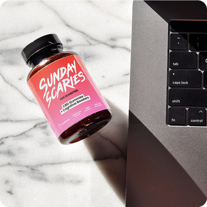 A bottle of Sunday Scaries CBD gummies for focus on a marble counter next to a laptop.
