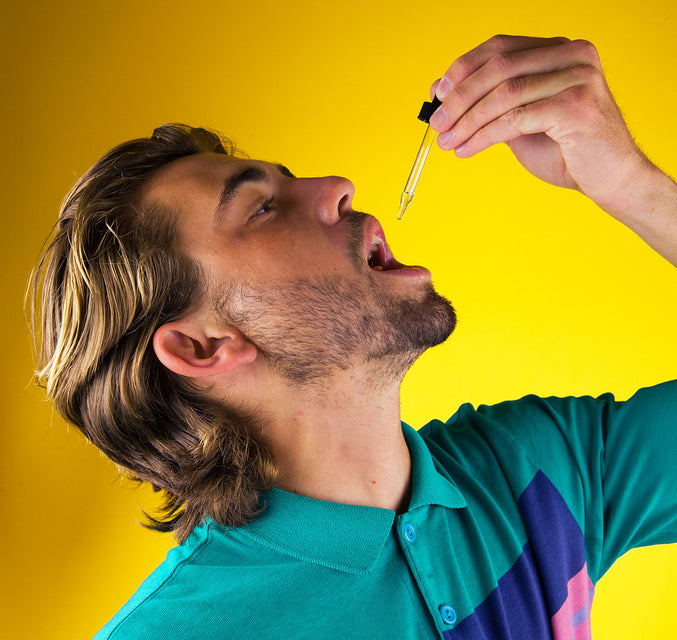 A man in a colorful polo shirt tilts his head back to consume some full spectrum CBD oil