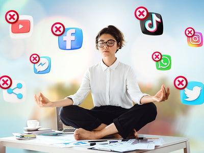 A woman meditates in lotus pose on her desk with her eyes closed while a bunch of x'd out social media apps fly around her