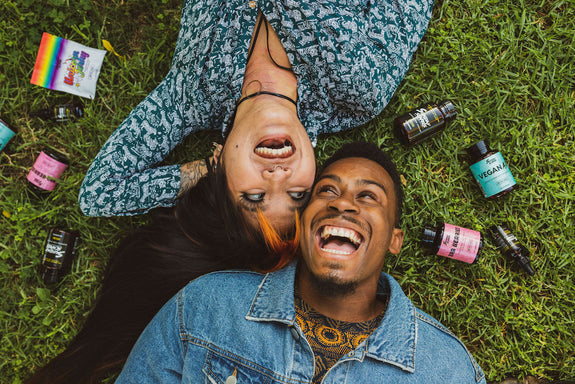 A man and a woman lie down on the grass smiling, surrounded by Sunday Scaries products