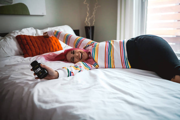 A girl is happily lying on the bed while holding a bottle of Sunday Scaries CBD Gummies