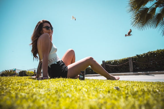 A woman relaxes in a park next to the beach with a bottle of Sunday Scaries showing the benefits of THC gummies