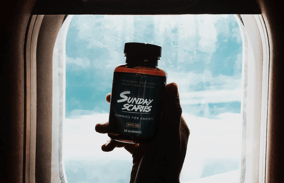 A Sunday Scaries gummies bottle in front of an airplane window showing you can take CBD edibles on an airplane