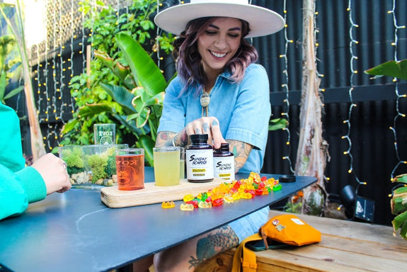 A woman holds a bottle of Sunday Scaries showing her friend what CBD does in THC edibles