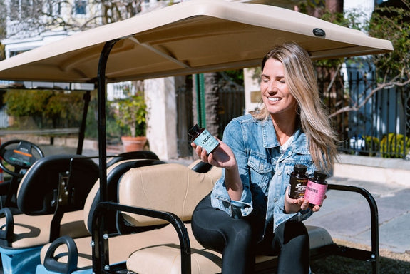 A woman in a golf cart holds up a CBD product in one hand and CBG products in the other showing the differences