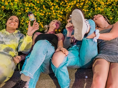 Four ladies lay on the ground laughing, holding bottles of Delta-9 gummies and THC gummies to show the difference