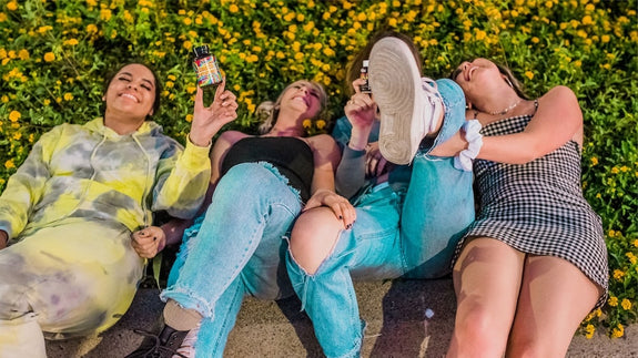 Four ladies lay on the ground laughing, holding bottles of Delta-9 gummies and THC gummies to show the difference