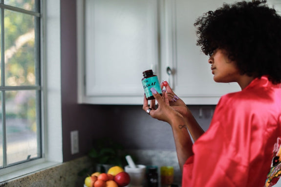 A woman checks the back of the label of Vegan AF in front of her cabinet to check when CBD gummies expire