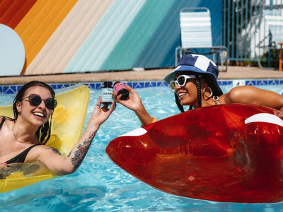 Two woman in a pool clank CBD gummies bottles in a pool to show if full spectrum vs broad spectrum is better for anxiety