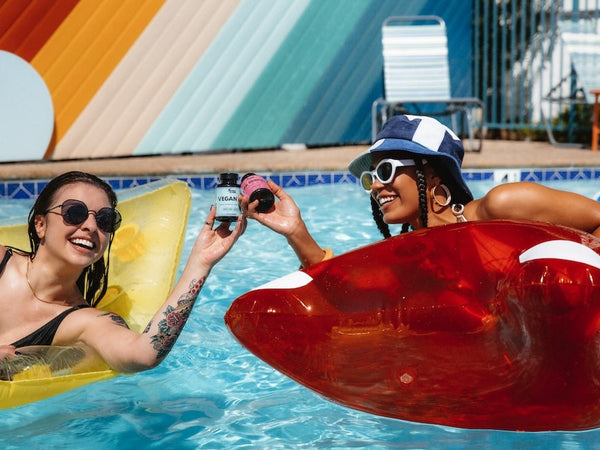 Two woman in a pool clank CBD gummies bottles in a pool to show if full spectrum vs broad spectrum is better for anxiety