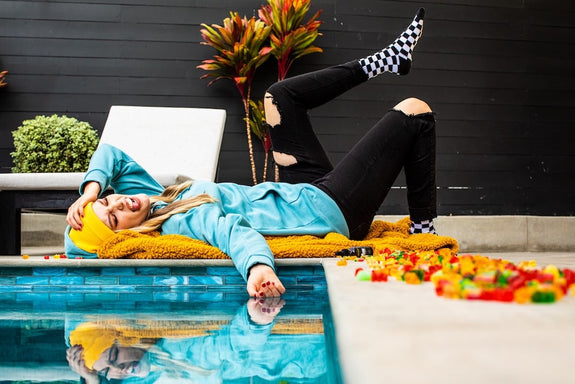 A woman lies hungover next to her pool and a pile of hangover gummies with CBD