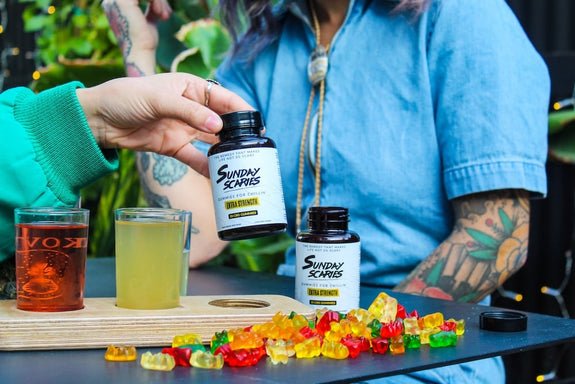 Two women at a table chat about how long CBD gummies last while holding a bottle of Sunday Scaries