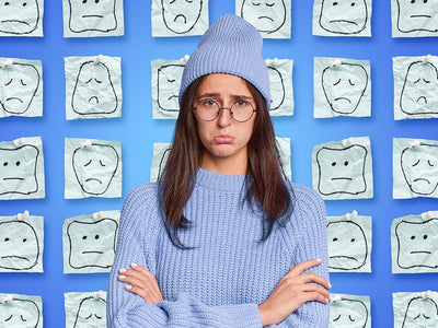 A woman looks depressed in front of a blue backdrop of sad faces answering the question 