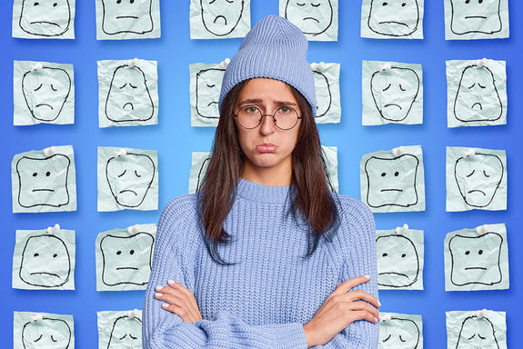 A woman looks depressed in front of a blue backdrop of sad faces answering the question "What are Sunday Blues?"