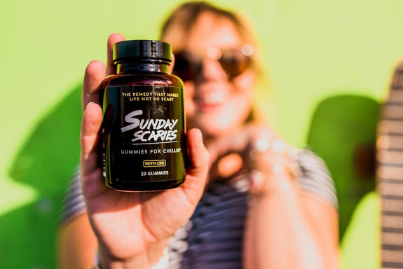 A woman holds up a bottle of Sunday Scaries while smiling, showing what CBD gummies do.