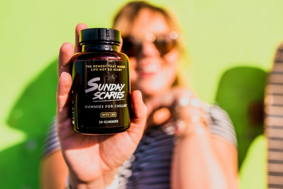 A woman holds up a bottle of Sunday Scaries while smiling, showing what CBD gummies do. 