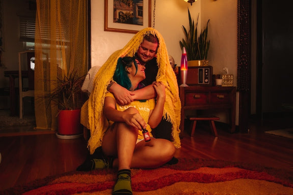 A boyfriend with a blanket over his head hugs his girlfriend and tells her what strength CBD oil to use for sleep