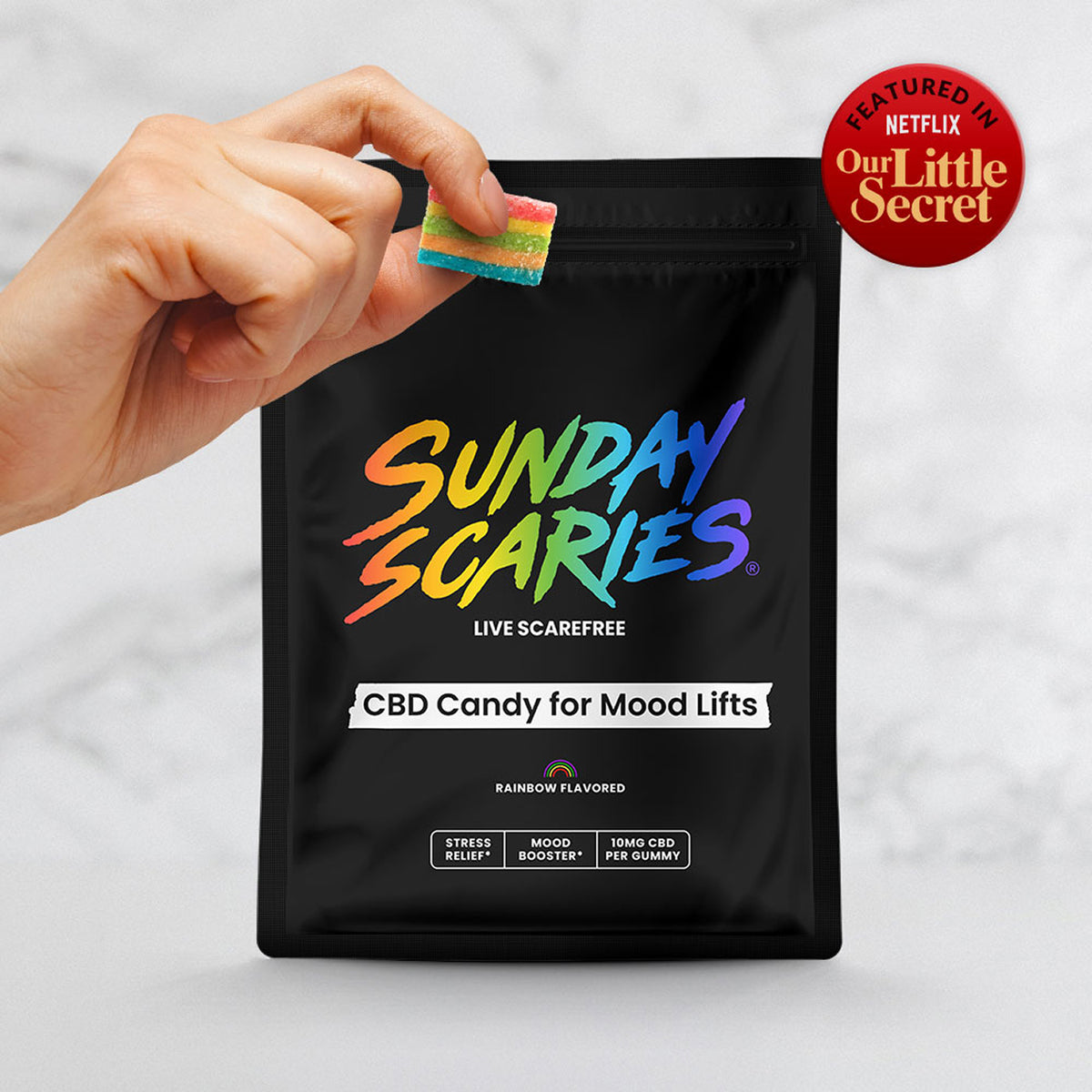 Black bag labeled 'Sunday Scaries' with colorful text, a hand holding a gummy candy and a badge showing it was featured in the Netflix movie "Our Little Secret"