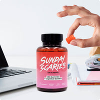 A hand holds a pink CBD focus gummy on a work desk next to a computer