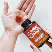 A person hands hold the Sunday Scaries mushroom gummy bottle in one and a triangle single gummy in the other